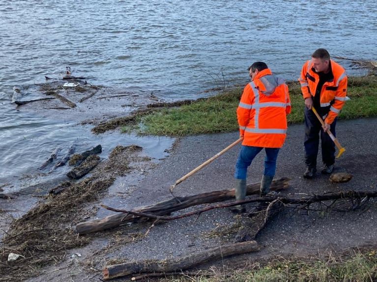 Mannen in oranje jassen verwijderen takken uit de rivier
